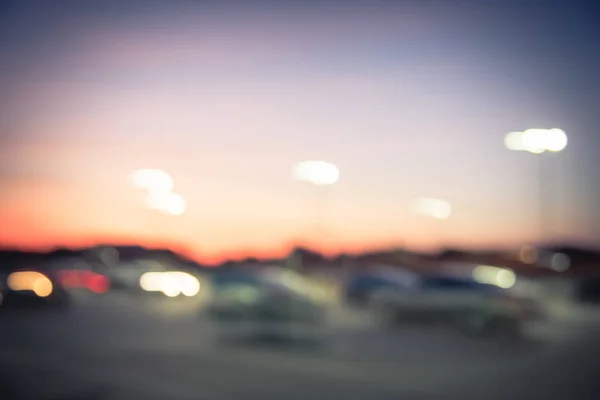 Blurred abstract parking lot at modern commercial strip in Irving, Texas, USA. Exterior mall shopping center complex with row of cars in outdoor uncovered parking, bokeh light poles in background