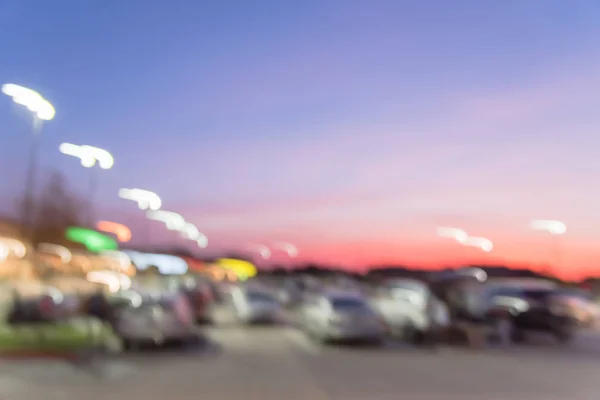 Abstract blurred exterior of modern commercial strip in Irving, Texas, US at sunset. Shopping center row of cars in outdoor uncovered parking lots, bokeh of retail store, light poles in background