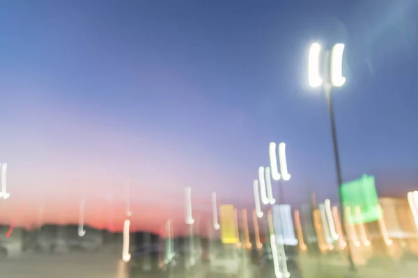 Abstract blurred exterior of modern commercial strip in Irving, Texas, US at sunset. Shopping center row of cars in outdoor uncovered parking lots, bokeh of retail store, light poles in background