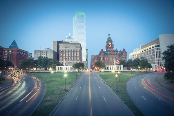 Винтажный тон прекрасный вид на небоскребы Далласа и легкий трафик над Дили Плаза, место убийства JKF. Skyline и городской транспорт в "синий час"
