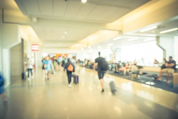 Defocused blurry people walking with luggage near terminal waiting area at American airport. Abstract blurred passengers or tourist with bag. Defocused traveler walk away at hallway, back view