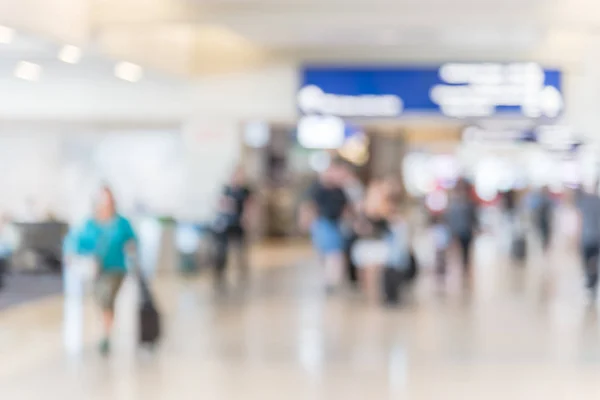 Blurred background passengers or tourist walking at airport hallway with Illuminated direction sign. Motion blurry people walk away with luggage at American terminal. Travel and transportation concept