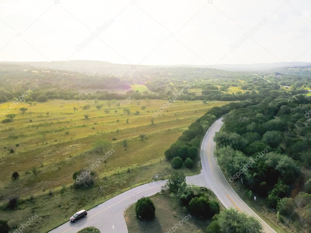 Aerial view green rolling hill landscape with scenic drive in Hill Country, West Texas, USA. Horizontal shot countryside and farmland, ranch flyover, blue sky