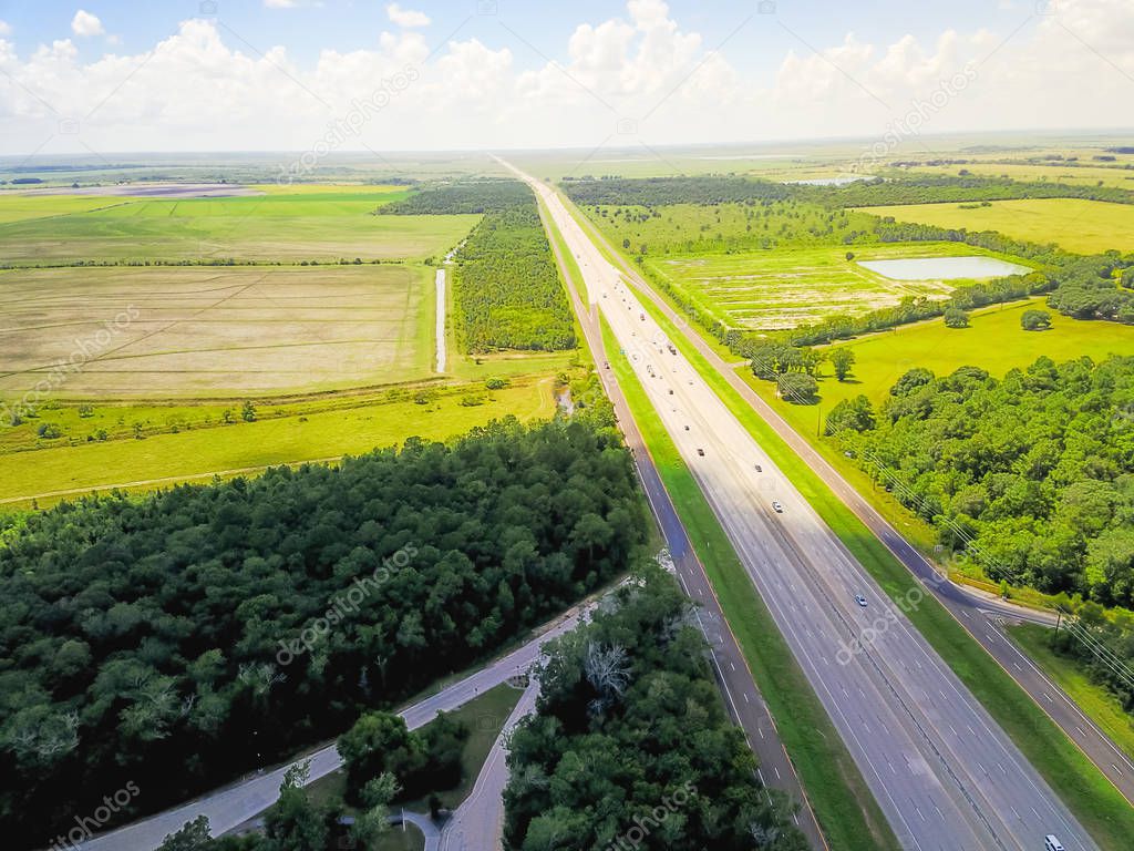 Aerial horizontal panorama view of endless Interstate 10 highway running through scenery of the Southern United States. Straight road flyover surrounded by green oak trees under cloud blue sky