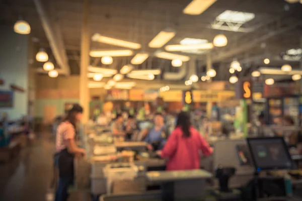 Blurred cashier line of people check-out counter. Customers paying credit card to store clerks in supermarket. Staff assisting, cashier register, computer on sales counter, checkout payment terminal