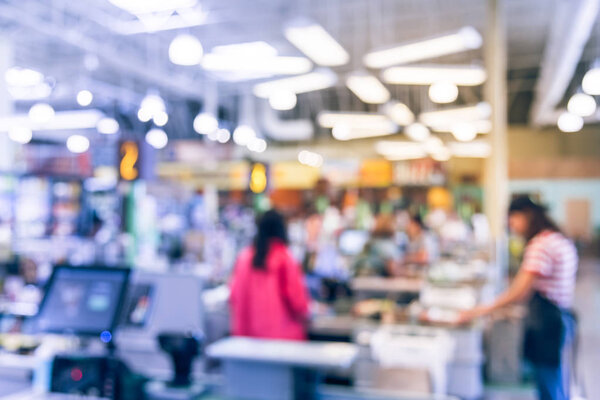 Blurred cashier line of people check-out counter. Customers paying credit card to store clerks in supermarket. Staff assisting, cashier register, computer on sales counter, checkout payment terminal