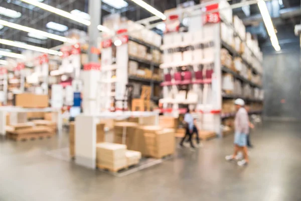Blurred customers shopping in large furniture warehouse with row of aisles and bins from floor to ceiling. Defocused background industrial storehouse interior. Inventory, wholesale, logistic, export