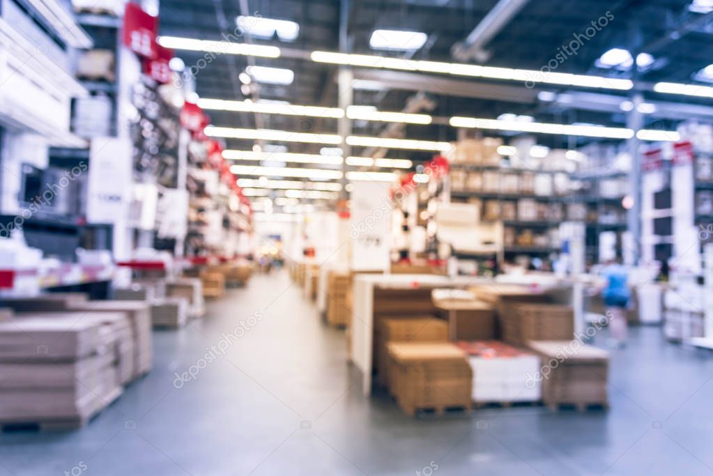 Blurred customers shopping in large furniture warehouse with row of aisles and bins from floor to ceiling. Defocused background industrial storehouse interior. Inventory, wholesale, logistic, export