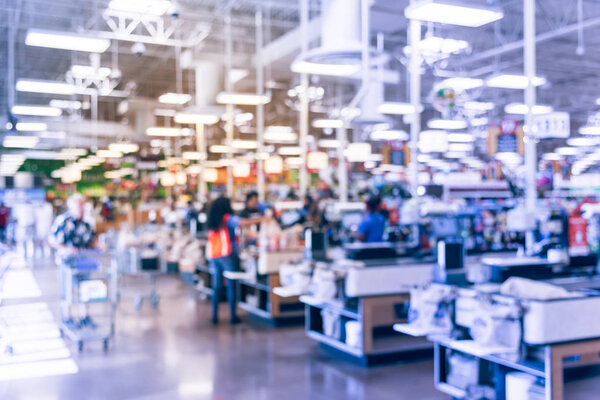 Blur image cashier with line of people at check-out counter. Customers paying with credit card to store clerks, employee help to bag groceries. Cashier register, computer, checkout payment terminal.