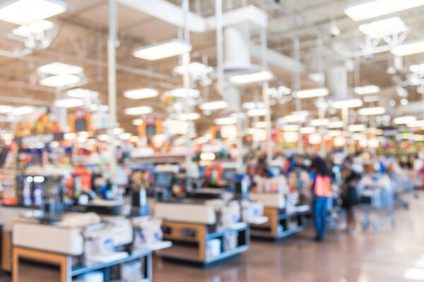 Blur image cashier with line of people at check-out counter. Customers paying with credit card to store clerks, employee help to bag groceries. Cashier register, computer, checkout payment terminal.
