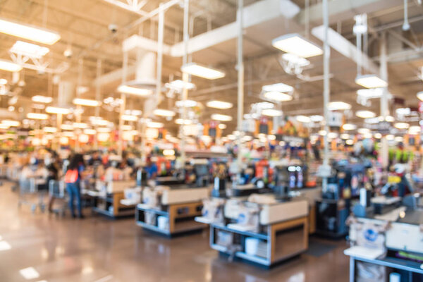 Blur image cashier with line of people at check-out counter. Customers paying with credit card to store clerks, employee help to bag groceries. Cashier register, computer, checkout payment terminal.