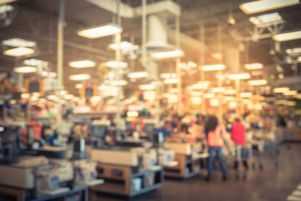 Blur image cashier with line of people at check-out counter. Customers paying with credit card to store clerks, employee help to bag groceries. Cashier register, computer, checkout payment terminal.