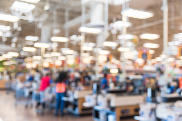 Blur image cashier with line of people at check-out counter. Customers paying with credit card to store clerks, employee help to bag groceries. Cashier register, computer, checkout payment terminal.