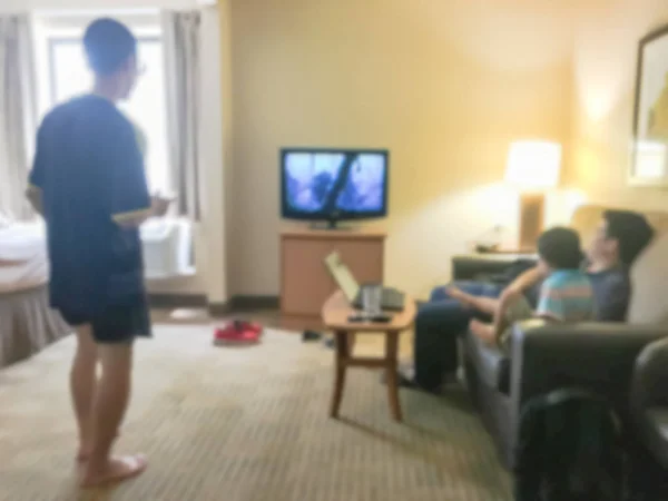 Blurred rear view of an Asian family relaxing on a sofa and watching TV at American hotel