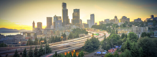Panoramic view Seattle skylines and rush hour traffic on highway I-90 and I-5 interchange. Nearby density of homeless tents, tiny shelter in trees foreground on the left. Problem of urban life concept