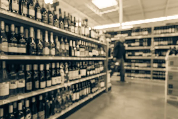 Vintage tone blurred customer shopping at wine shelves with price tags on display at store in USA. Defocused rows of liquor bottles on supermarket shelf. Alcoholic beverage abstract background