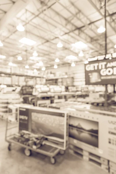 Vintage tone blurred TVs shopping at wholesale club. Television retail shop, row of big screen, smart TVs display on shelves and on flatbed cart. Defocused large warehouse technology aisle bokeh light