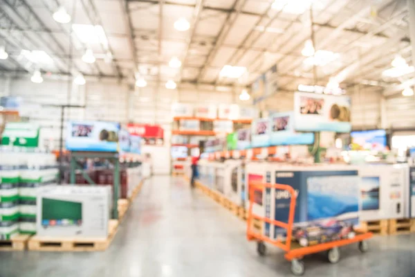 Blurred TVs shopping at large wholesale club. Television retail shop, row of big screen, smart TVs display on shelves. Customers browsing to select and use flatbed cart to carry TV to checkout counter