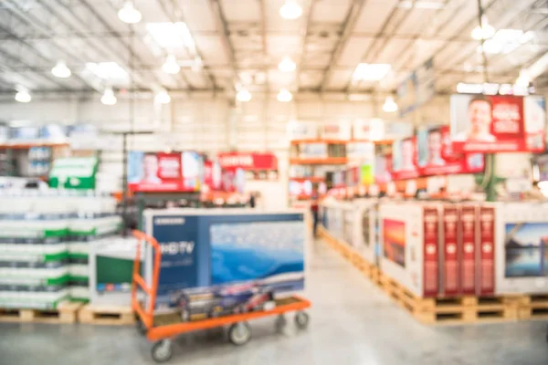 Blurred TVs shopping at wholesale club. Television retail shop, row of big screen, smart TVs display on shelves and on flatbed cart. Defocused large warehouse interior technology aisle bokeh light.