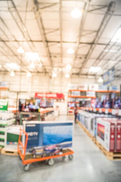 Blurred TVs shopping at large wholesale club. Television retail shop, row of big screen, smart TVs display on shelves. Customers browsing to select and use flatbed cart to carry TV to checkout counter