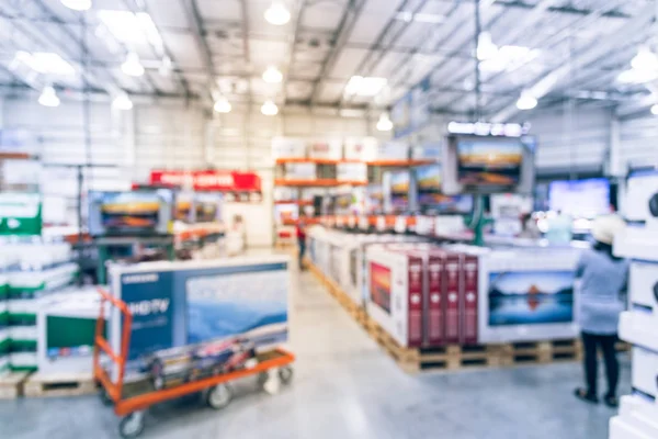 Blurred TVs shopping at large wholesale club. Television retail shop, row of big screen, smart TVs display on shelves. Customers browsing to select and use flatbed cart to carry TV to checkout counter