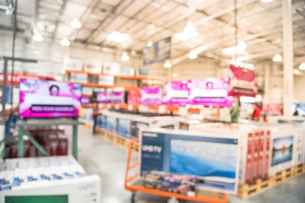 Blurred TVs shopping at large wholesale club. Television retail shop, row of big screen, smart TVs display on shelves. Customers browsing to select and use flatbed cart to carry TV to checkout counter