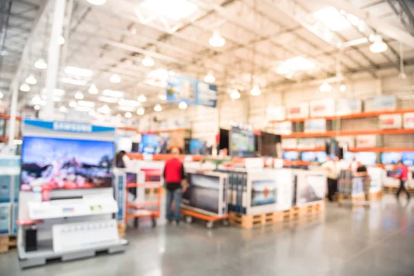 Blurred TVs shopping large wholesale club. Television retail shop, row of big screen, smart TVs display on shelves. Store staff help customers select and use flatbed cart carry TV to checkout counter.