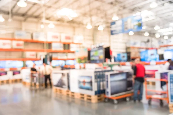 Blurred TVs shopping large wholesale club. Television retail shop, row of big screen, smart TVs display on shelves. Store staff help customers select and use flatbed cart carry TV to checkout counter.