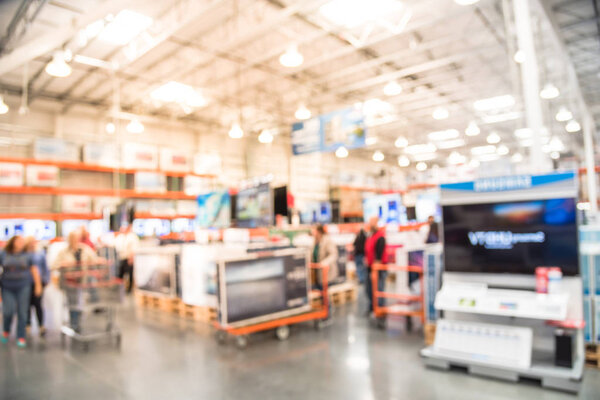 Blurred TVs shopping large wholesale club. Television retail shop, row of big screen, smart TVs display on shelves. Store staff help customers select and use flatbed cart carry TV to checkout counter.