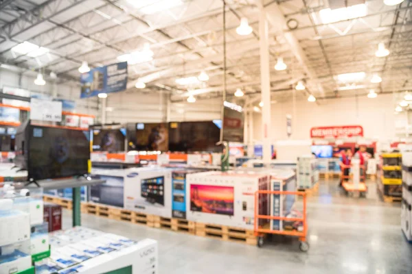 Blurred TVs shopping large wholesale club. Television retail shop, row of big screen, smart TVs display on shelves. Store staff help customers select and use flatbed cart carry TV to checkout counter.