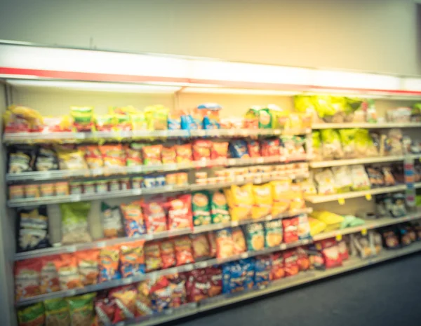 Blurred image of snacks and canned chips aisle in store at Humble, Texas, US. Wide perspective view shelves variety of snacks, defocused blurry background bokeh light in supermarket. Business concept.