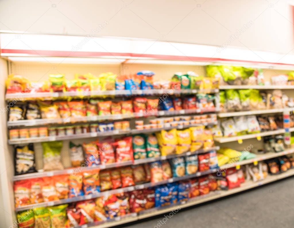 Blurred image of snacks and canned chips aisle in store at Humble, Texas, US. Wide perspective view shelves variety of snacks, defocused blurry background bokeh light in supermarket. Business concept.