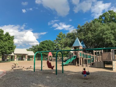 Arka görünümü Asyalı çocuk gür ABD daha büyük ağaçların altında genel ahşap çocuk oyun alanı ile lastik ve sandalye salıncaklar oynuyorsun. Oyun set yapısı yaz tarafından çevrili yeşil, bulut mavi gökyüzü yaprakları