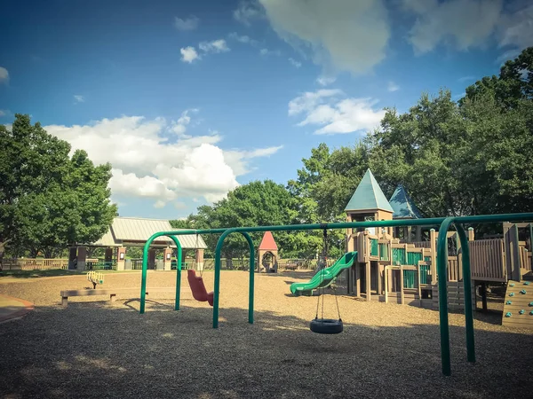 コッペル テキサス 米国で大きな木の緑豊かな下公共木造子供遊び場ではタイヤと椅子がブランコします 夏葉の緑に囲まれたセットの構造を再生し 青い空の雲 — ストック写真