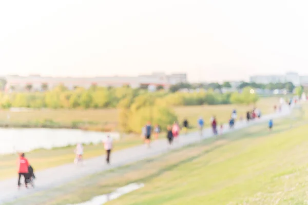 Blurred group of energetic people jog, walk, run, push stroller and bike through pathway with green tree, grass in city park at Houston, Texas, US. Abstract motion outdoor exercise. Healthy lifestyle