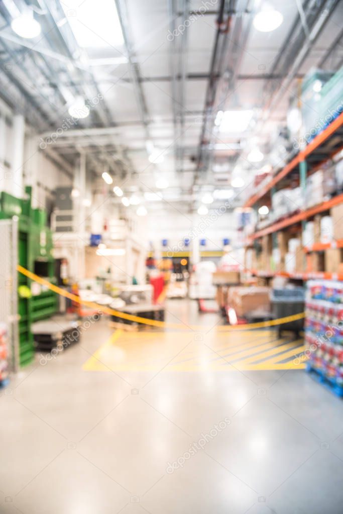 Blurred large warehouse with worker stack goods with forklifts, pallet, flatbed cart. Defocused industrial distribution interior row aisles, shelves from floor to ceiling. Inventory, wholesale concept