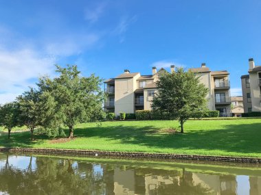 Mirror reflection of typical multistorey riverside apartment housing complex surrounded by mature trees in Irving, Texas, USA. clipart