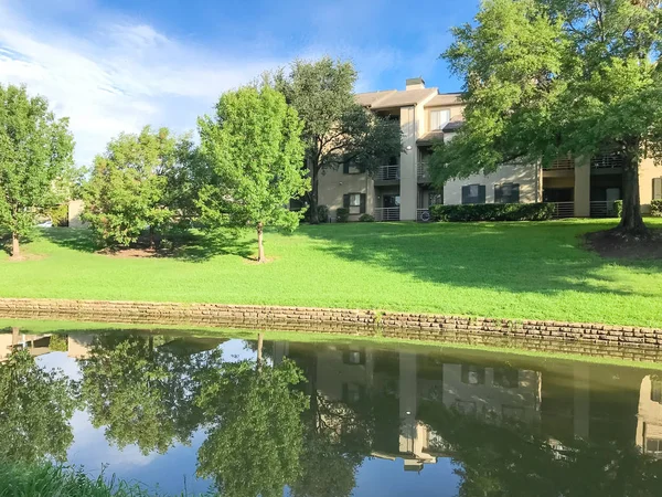 Mirror reflection of typical multistorey riverside apartment housing complex surrounded by mature trees in Irving, Texas, USA.