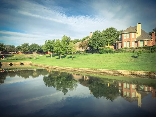 Mirror reflection of typical riverside houses surrounded by mature trees in Irving, Texas, USA.