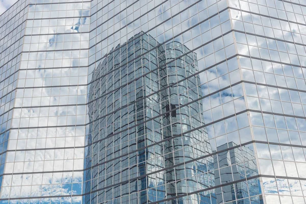 Clouds and mirror building reflected in windows of modern office workspace. Steel light blue background of glass high-rise commercial skyscraper, the city of future concept