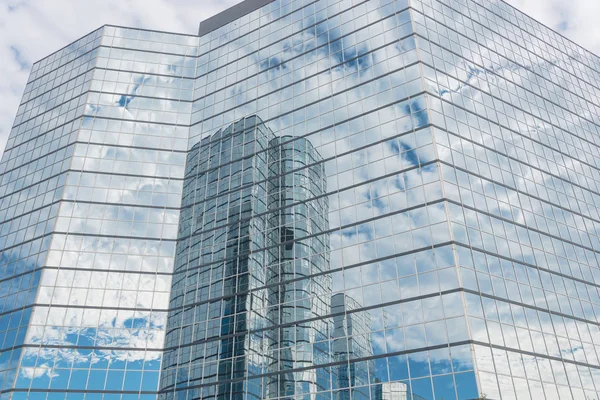 Clouds and mirror building reflected in windows of modern office workspace. Steel light blue background of glass high-rise commercial skyscraper, the city of future concept