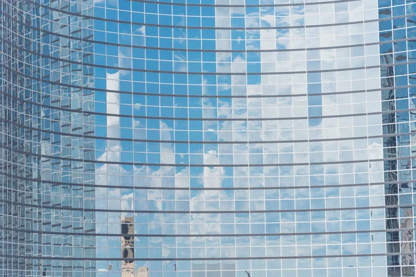 Clouds and mirror building reflected in windows of modern office workspace. Steel light blue background of glass high-rise commercial skyscraper, the city of future concept