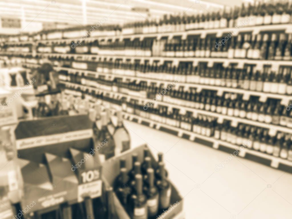 Color toned image, blurred wine aisle with price tags at grocery store in Texas, America. Defocused rows of red, white wine liquor bottles on supermarket shelf. Alcoholic beverage abstract background