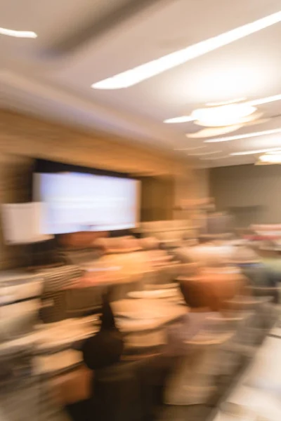 Blurred business seminar meeting with LED projector screen and speaker speech on stage. Defocused rear view audience in conference hall room, listening talk show in USA. Education, business concept