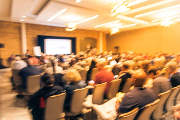 Blurred business seminar meeting with LED projector screen and speaker speech on stage. Defocused rear view audience in conference hall room, listening talk show in USA. Education, business concept