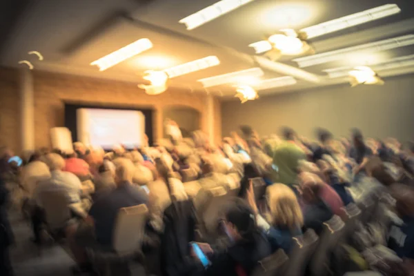 Blurred business seminar meeting with LED projector screen and speaker speech on stage. Defocused rear view audience in conference hall room, listening talk show in USA. Education, business concept