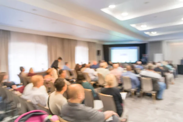 Blurred business seminar meeting with LED projector screen and speaker speech on stage. Defocused rear view audience in conference hall room, listening talk show in USA. Education, business concept