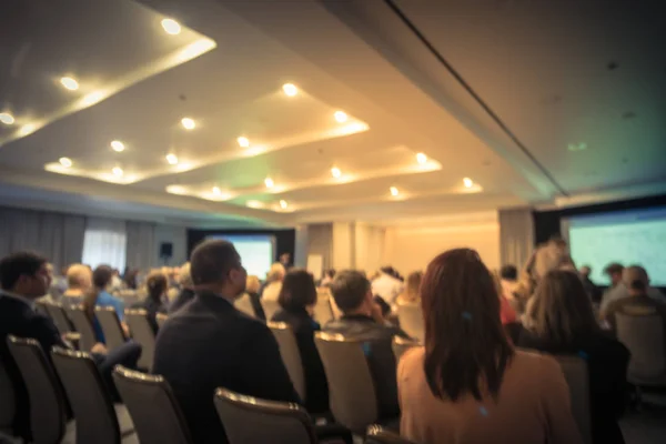 Vintage tone blurred business seminar meeting with LED projector screen, speaker speech on stage. Defocused rear view audience in conference hall room, listening talk show. Education, business concept