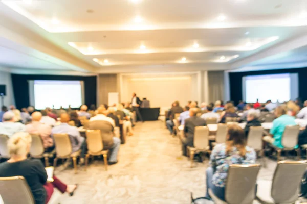 Vintage tone blurred business seminar meeting with LED projector screen, speaker speech on stage. Defocused rear view audience in conference hall room, listening talk show. Education, business concept