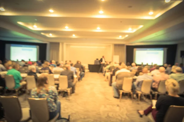 Vintage tone blurred business seminar meeting with LED projector screen, speaker speech on stage. Defocused rear view audience in conference hall room, listening talk show. Education, business concept